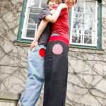 Bub und Frau in PIratenhosen, er in hellblauem Denim mit roter Tasche, sie in schwarzem Leinen mit rot weiß karierter Tasche